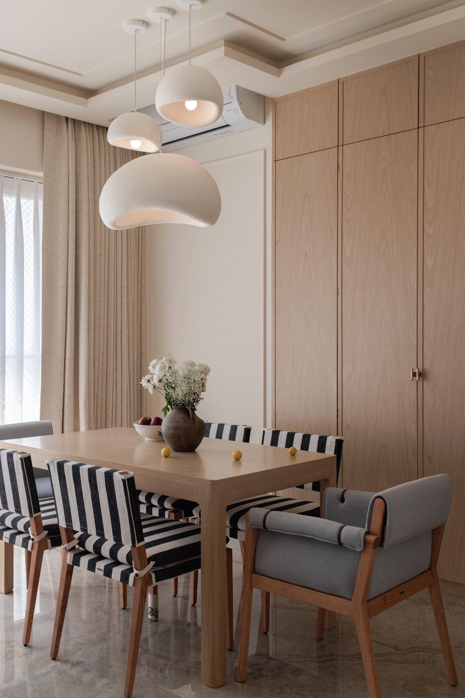The dining zone, with textured white pendants and striped upholstery introducing a graphic counterpoint to the timber palette