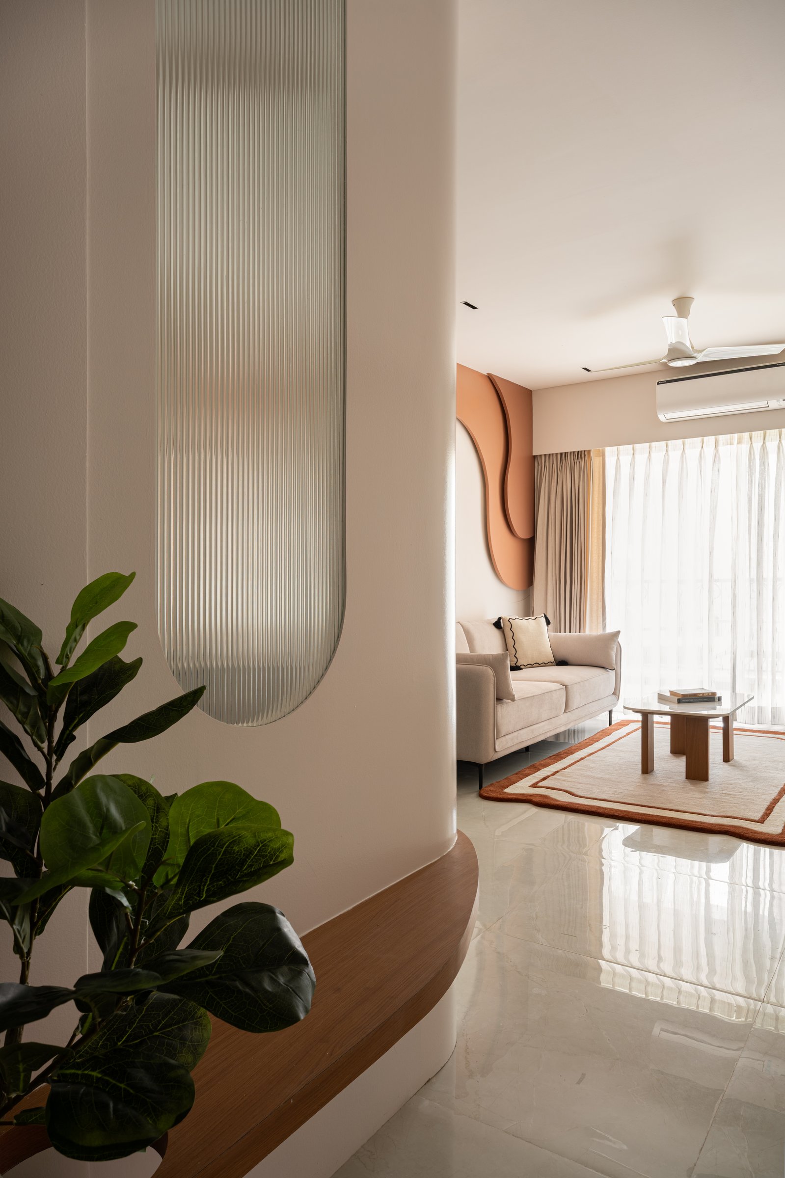 A glimpse from entry to living room: the sculptural terracotta wall announces itself beyond the fluted-glass screen