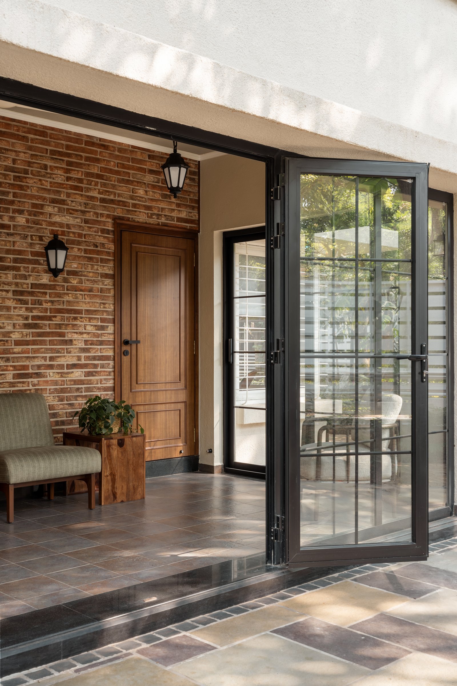 The verandah threshold, where exposed brick, a solid timber door, and steel-framed bi-fold glazing mediate between garden and interior