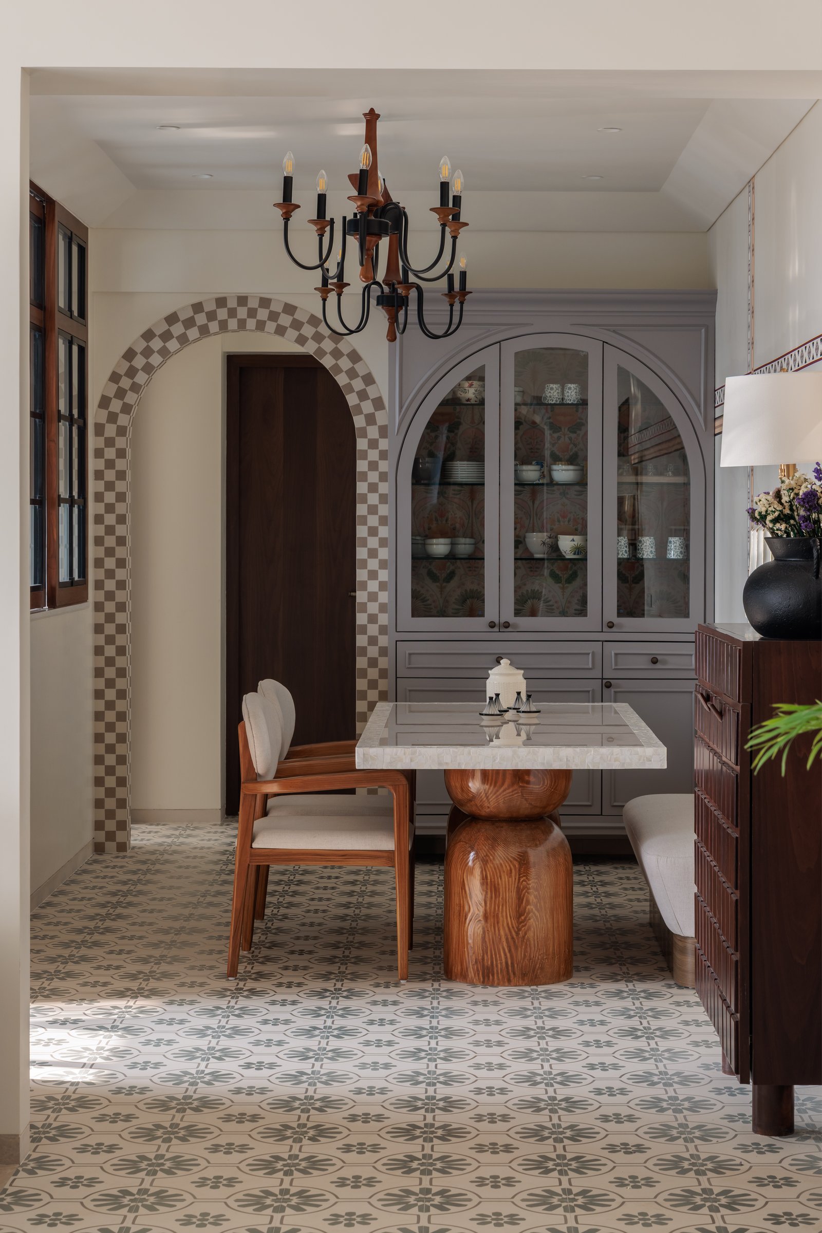 The dining area, where a sculptural timber-base table and an arched glass-fronted hutch create a distinct zone within the open plan