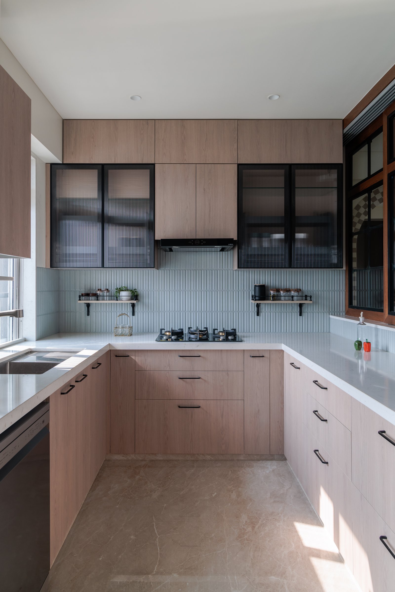 The kitchen steps into a cleaner register: light oak, ribbed tile, and fluted glass in black frames